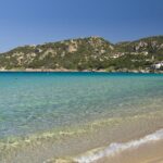 Una spiaggia della Costa Smeralda, con l'acqua trasparente e le colline di macchia mediterranea