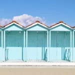 Una fila di cabine azzurre in legno sulla sabbia di uno stabilimento