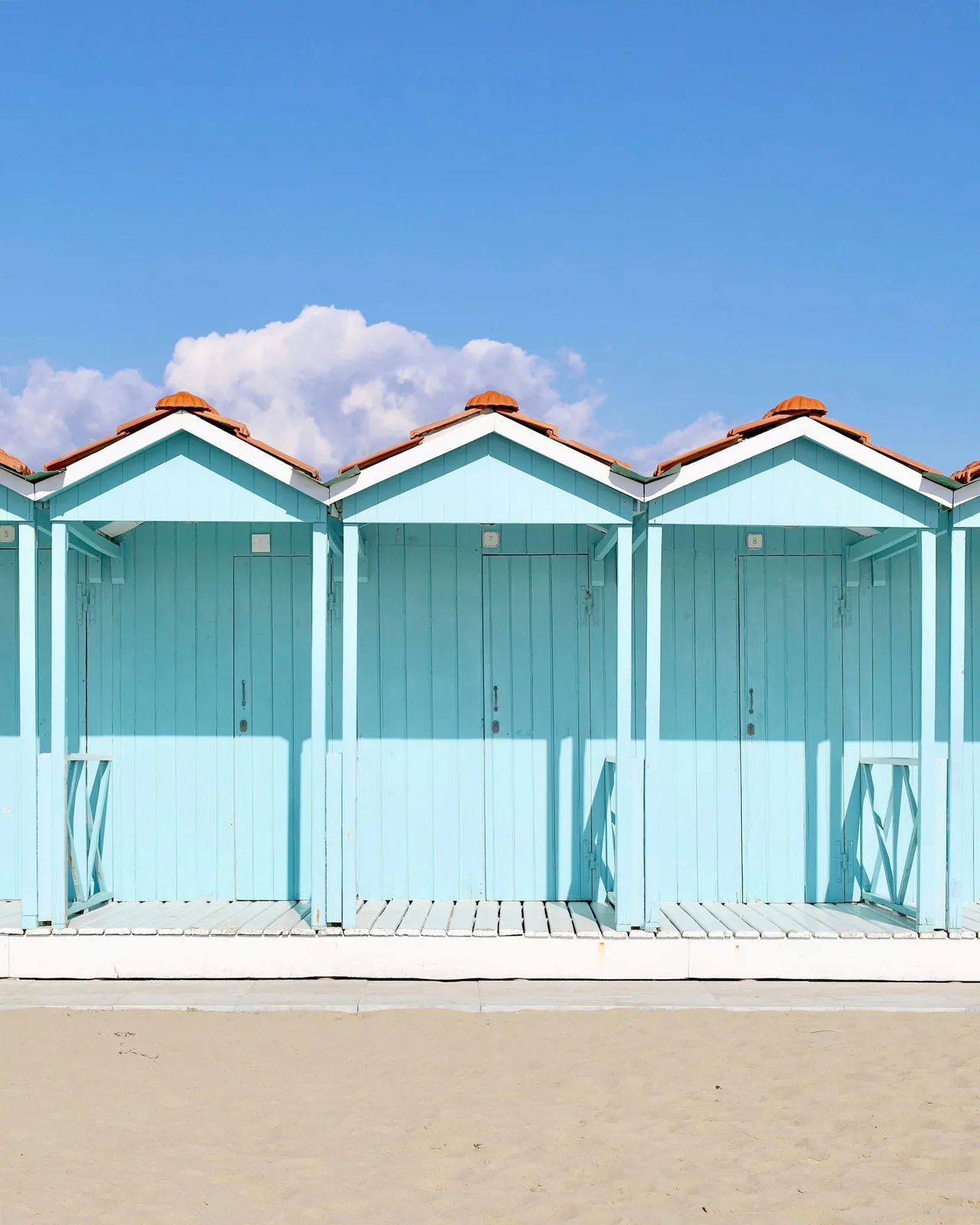 Una fila di cabine azzurre in legno sulla sabbia di uno stabilimento