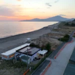 Uno stabilimento balneare sulla spiaggia al tramonto, ripreso dal drone, con la costa e le montagne sullo sfondo