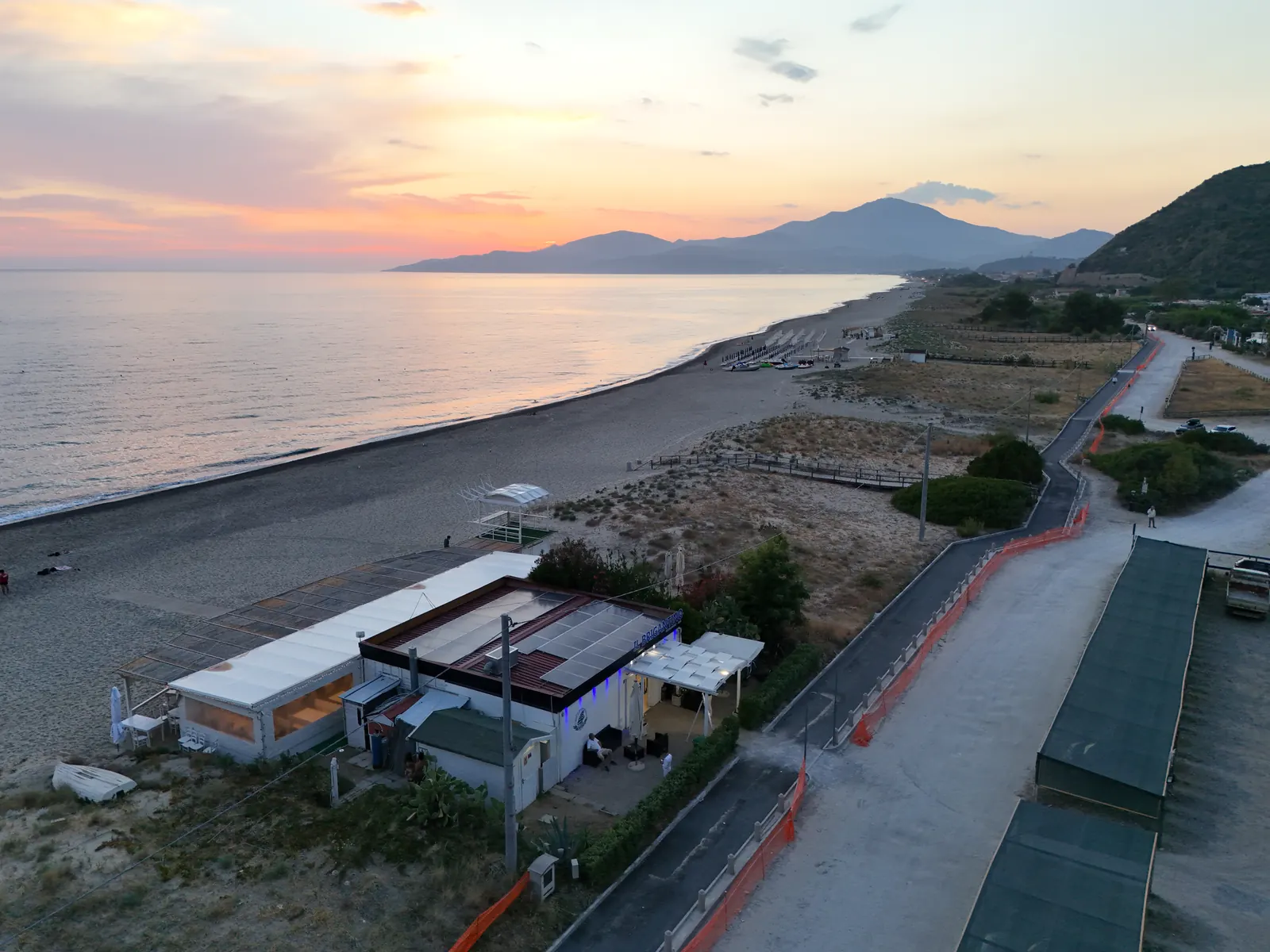 Uno stabilimento balneare sulla spiaggia al tramonto, ripreso dal drone, con la costa e le montagne sullo sfondo