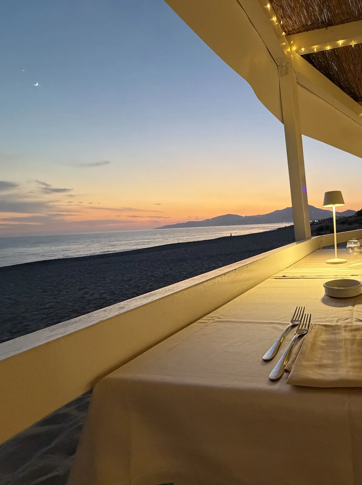 Un tavolo apparecchiato del ristorante sulla spiaggia, con il mare al tramonto
