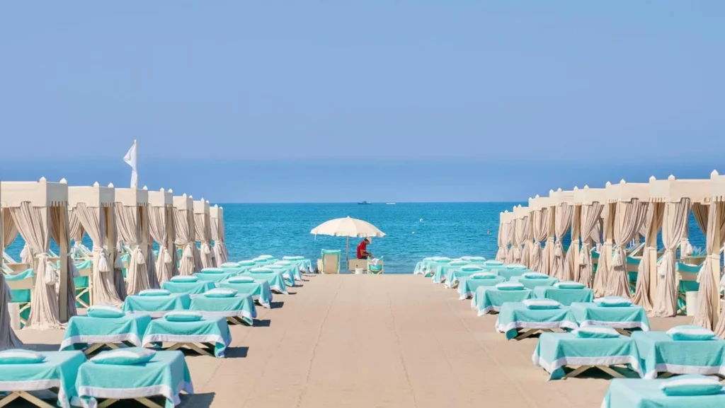 Due file di tende bianche e lettini turchesi verso il mare