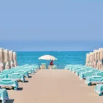 Due file di tende bianche e lettini turchesi verso il mare