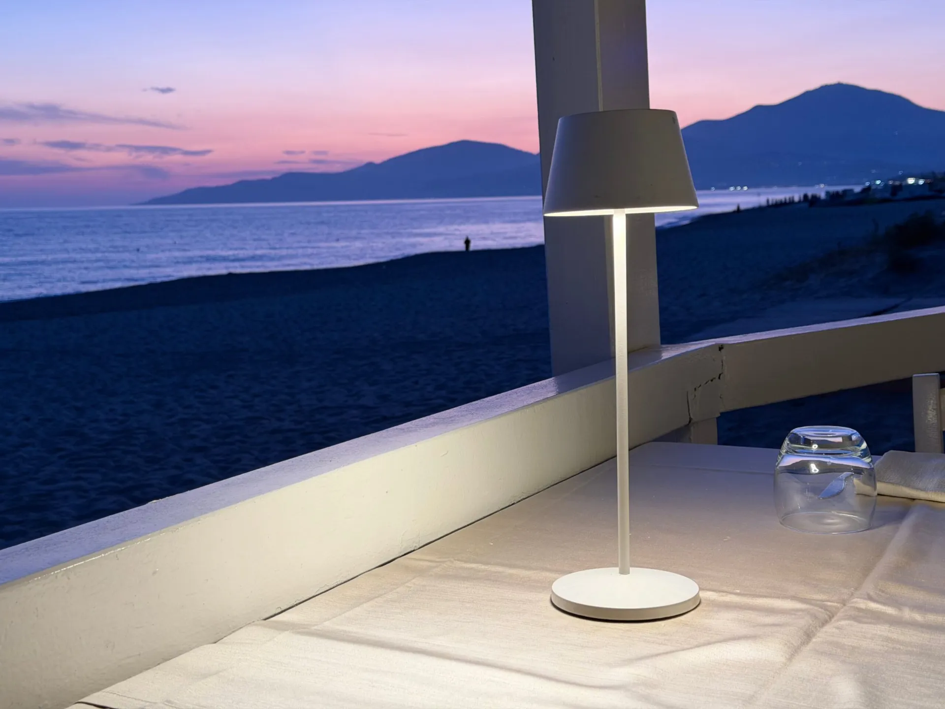 Un tavolo apparecchiato sulla terrazza di uno stabilimento balneare, al tramonto, con la spiaggia vuota sullo sfondo