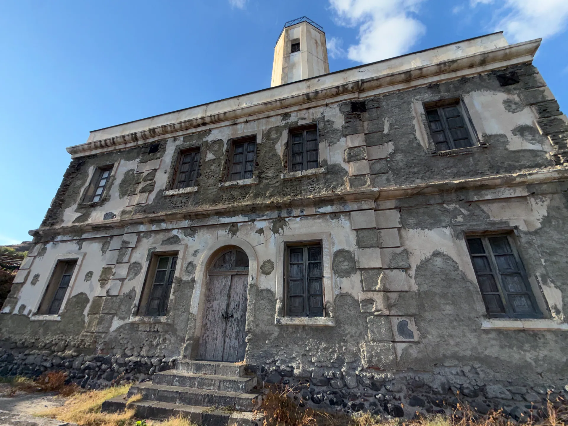 La facciata di un faro dello Stato in Sicilia con intonaco caduto e imposte chiuse