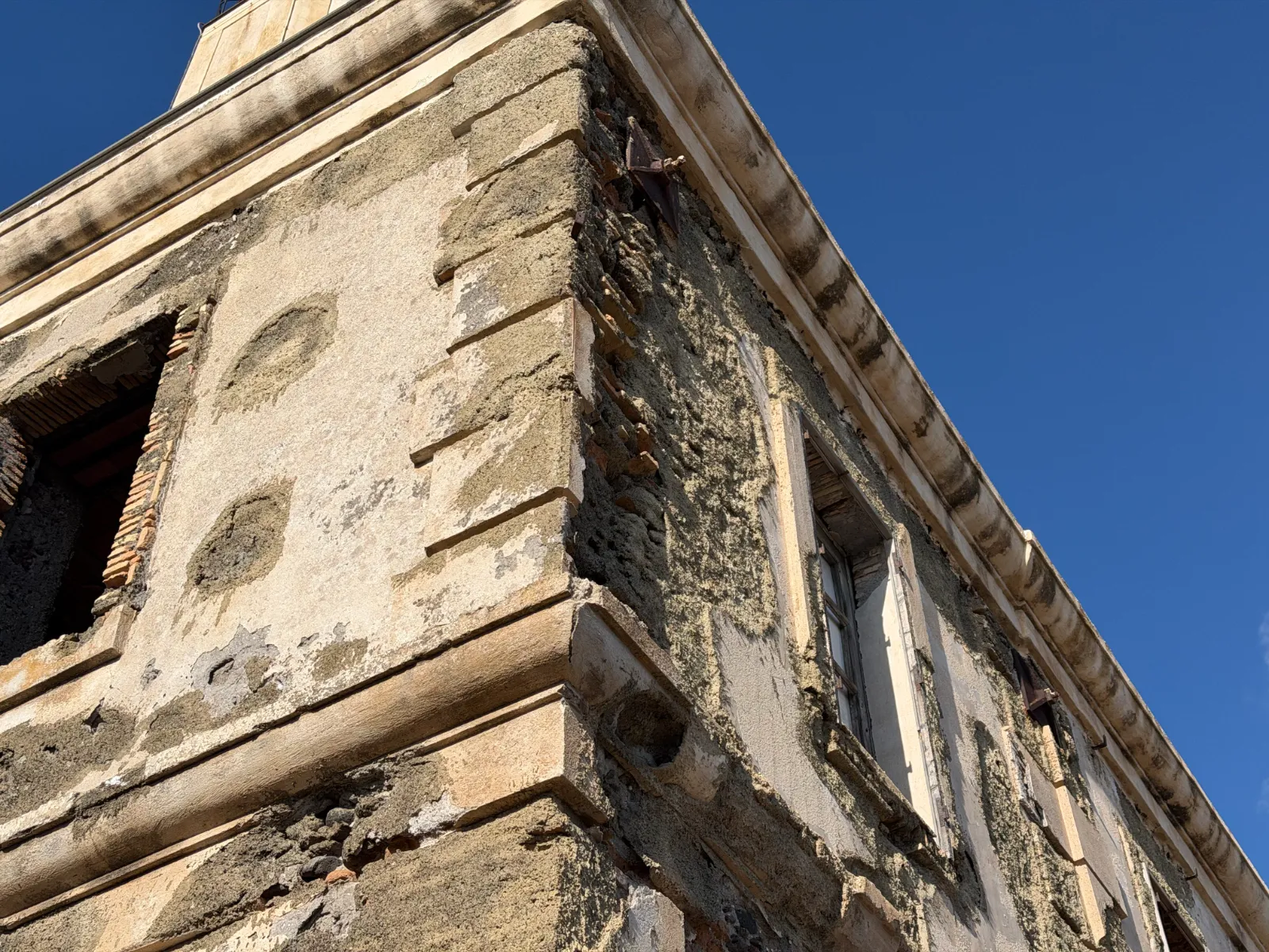 Spigolo di un faro abbandonato: intonaco caduto, mattoni a vista, ferro arrugginito