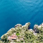 Il faro visto dall’alto sul promontorio, con il mare blu