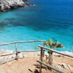 Una cala con l’acqua turchese e la staccionata di legno sugli scogli