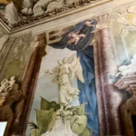Una figura alata dipinta fra colonne finte e un drappo blu