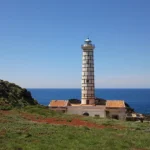 Il faro fra i prati e le rocce, con il mare aperto
