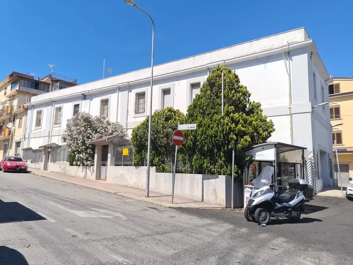 L’ex caserma bianca all’angolo della via, con gli alberi nel cortile