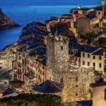 La Torre Capitolare illuminata la sera, fra i tetti del borgo e il porto