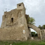 La torre in pietra con l’arco e la scala d’accesso