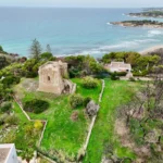 Torre Castelluccia vista dall'alto, sul prato davanti alla baia e alla spiaggia di Pulsano